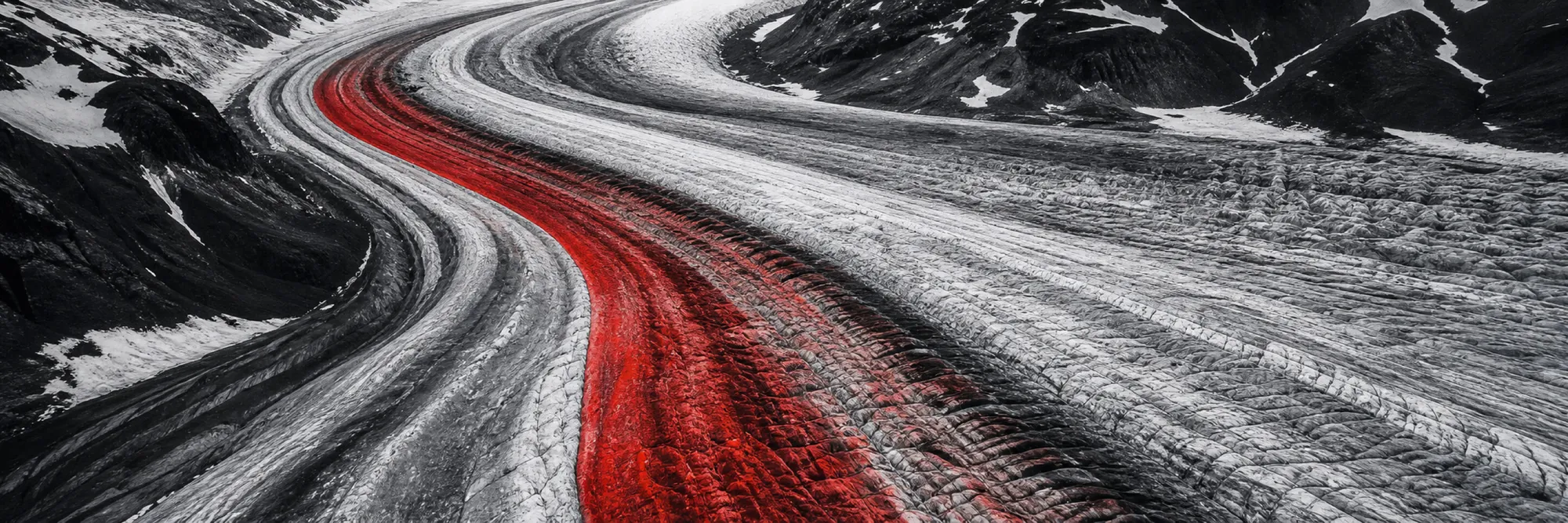 Monochrome glacier stream from the air, the medial moraine drawing a red band through the ice
